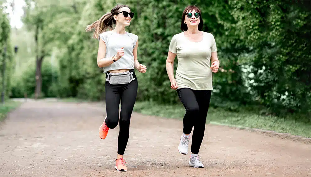 „Lifestyle-Aufnahme eines Paares beim gemeinsamen Joggen im herbstlichen Wald. Beide lächeln motiviert und tragen sportliche Laufkleidung. Das Bild unterstreicht die positiven Effekte von Bewegung auf die Stimmung und das Durchhaltevermögen während der Raucherentwöhnung mit Asmoken.