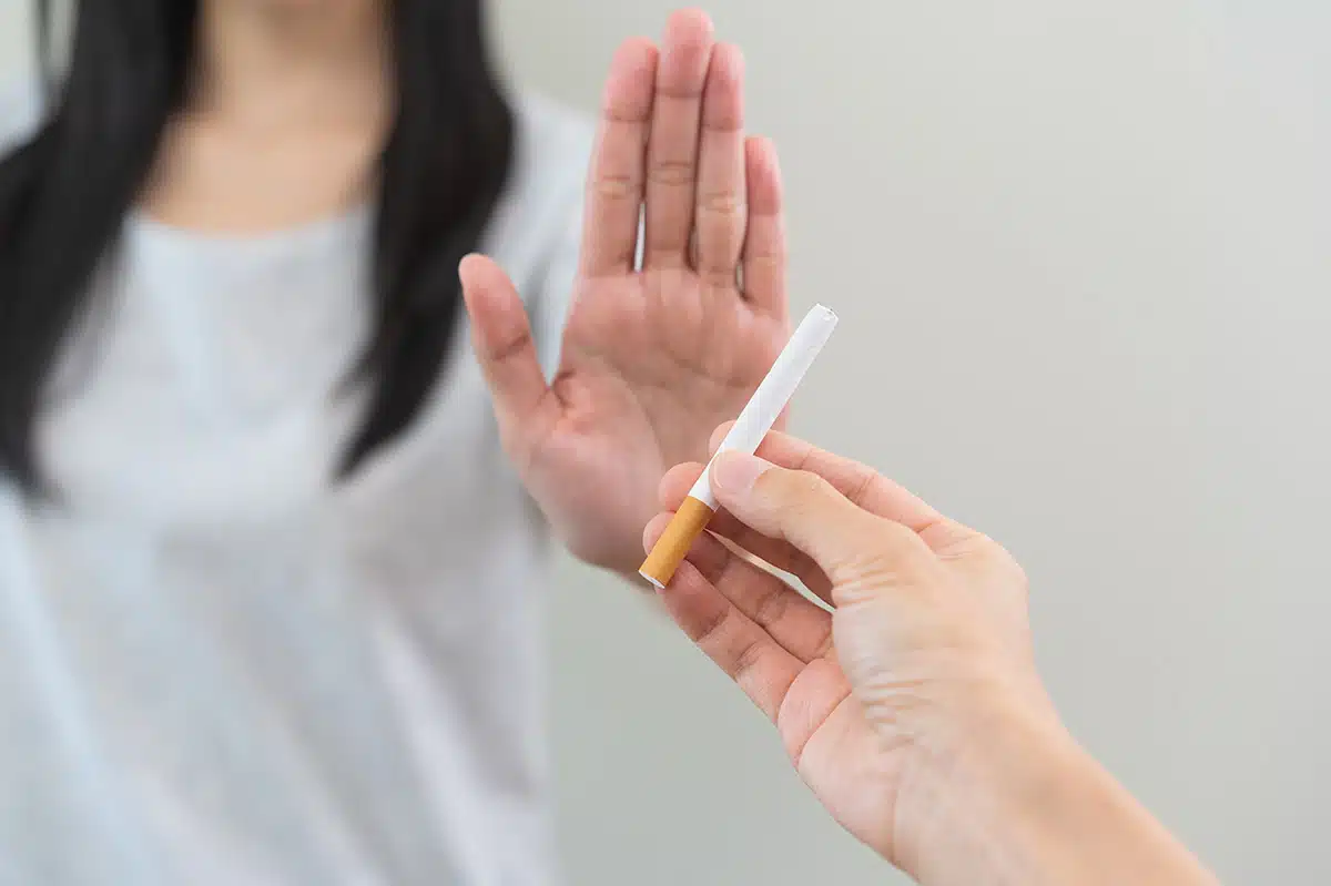 Nahaufnahme einer Person, die mit einer abweisenden Geste der flachen Hand eine angebotene Zigarette ablehnt. Das Bild symbolisiert die feste Entschlossenheit beim Rauchstopp und den erfolgreichen Umgang mit Versuchungen während der Raucherentwöhnung mit Asmoken.