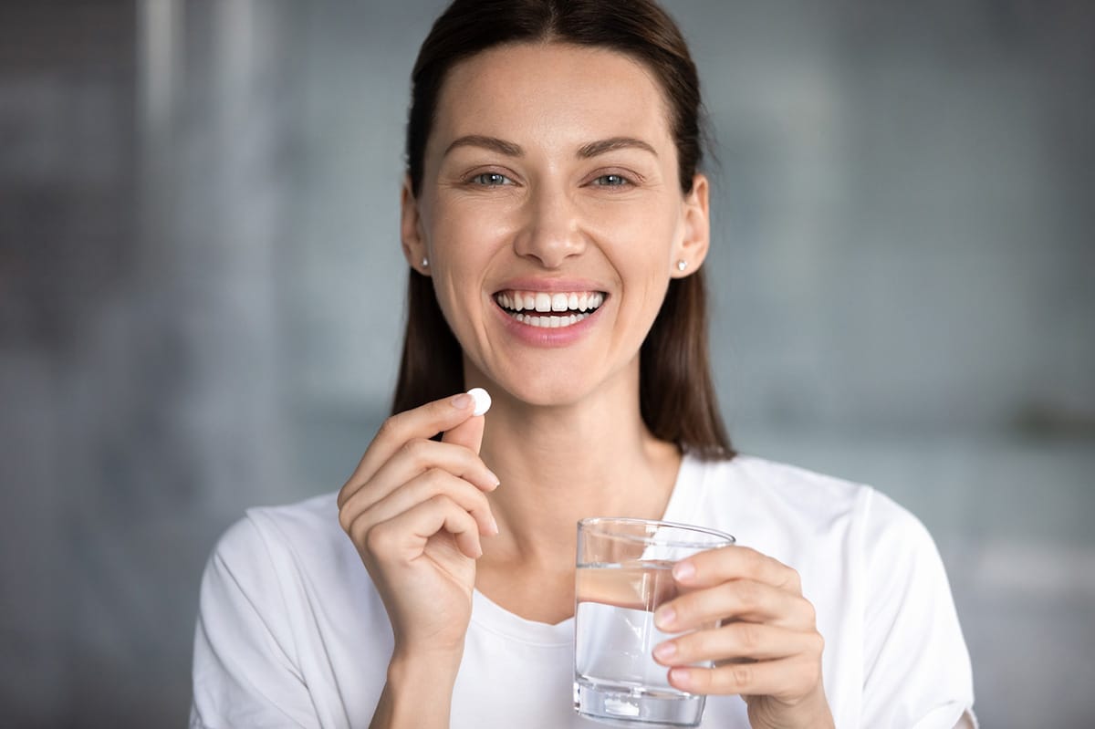 Frau mit Wasserglas und Tablette