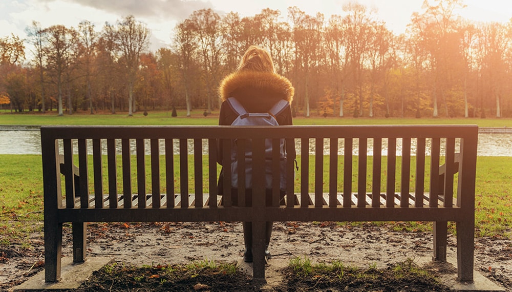Frau sitzt auf einer Bank, schaut auf Bäume, herbstliche Atmospähre